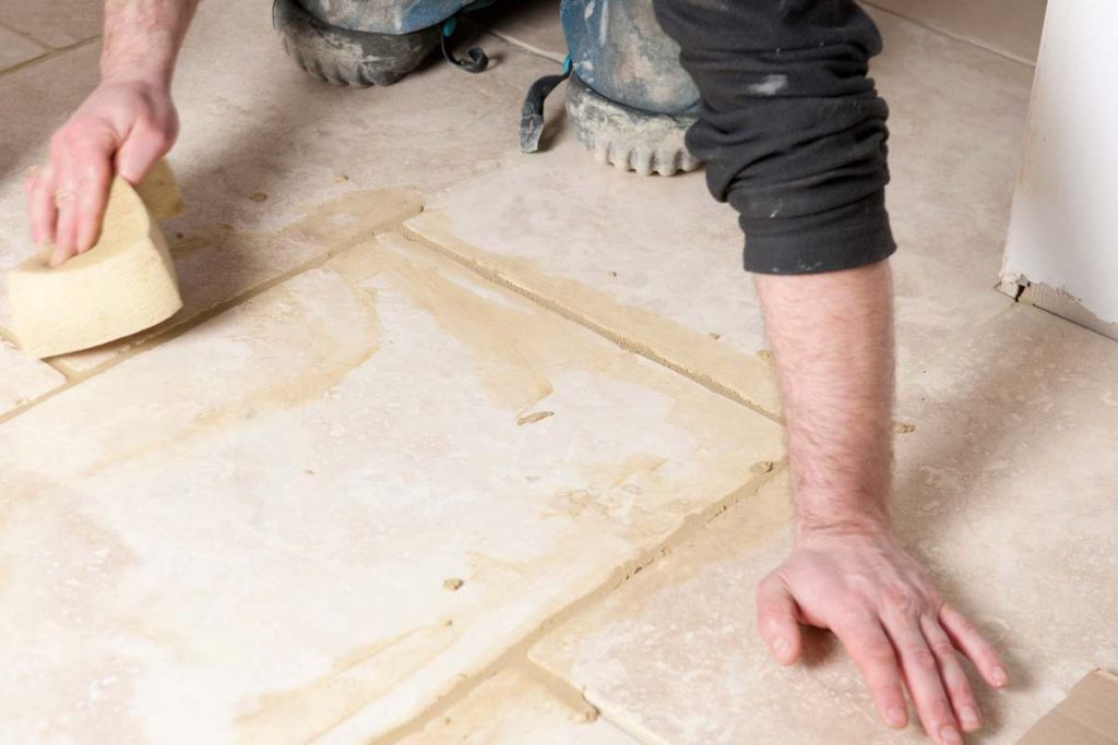 Person cleaning tiled floor grout using a natural cleaning solution and soft brush in an eco-conscious manner.