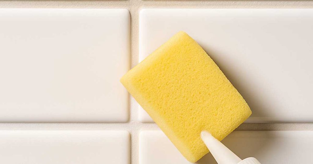 Close-up of grout sealing being applied between white subway tiles with an applicator sponge